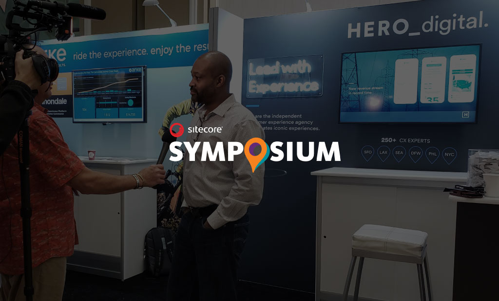 Sitecore Symposium logo over photo of Carl Agers being interviewed by Hero Digital booth.