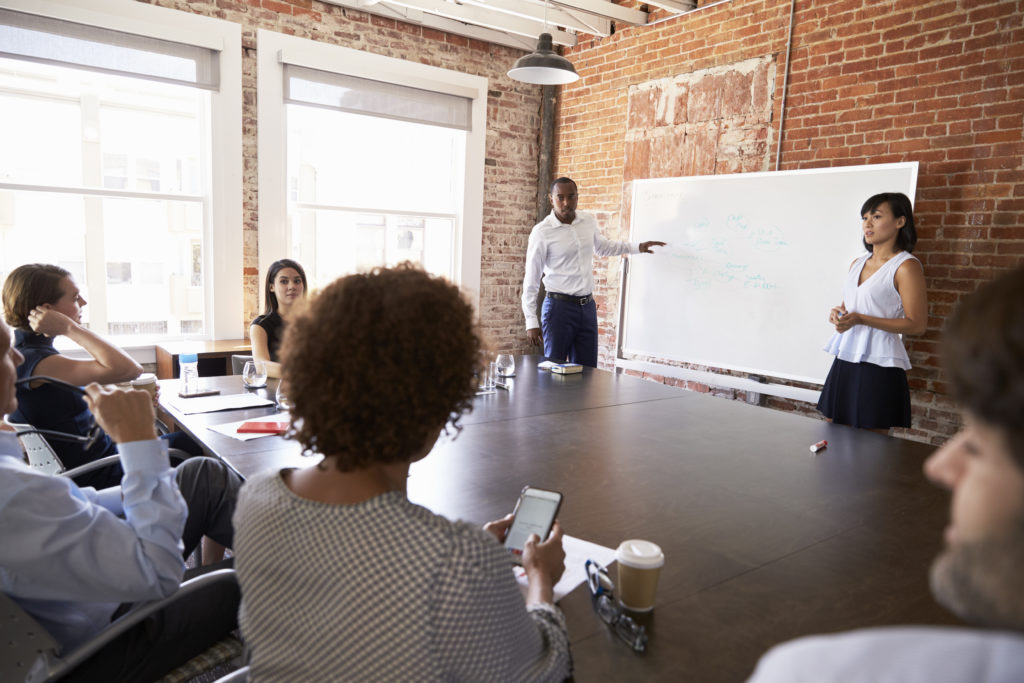 Businesspeople At Whiteboard Give Presentation In Boardroom