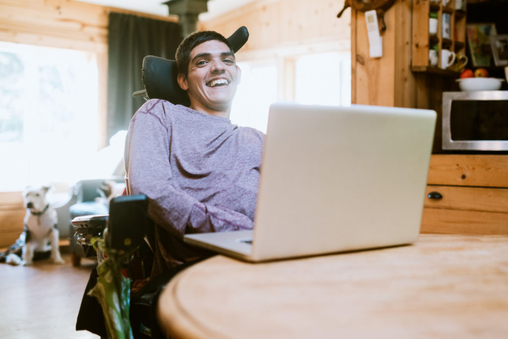 Man with cerebral palsy researches something on his laptop, using voice recognition assistive technology