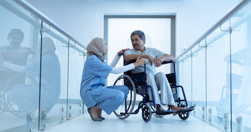 Female doctor in hijab interacting with male patient in wheelchair in the corridor at hospital