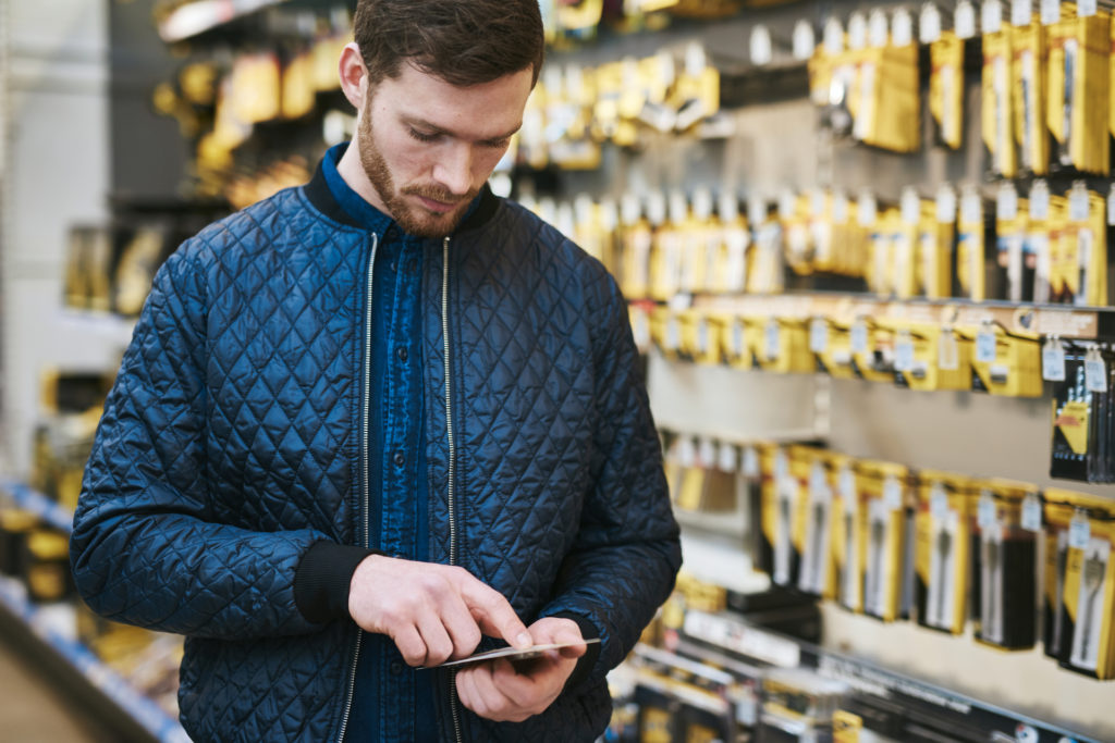 Young man checking a text message on his mobile phone as he shops in a hardware store for DIY supplies